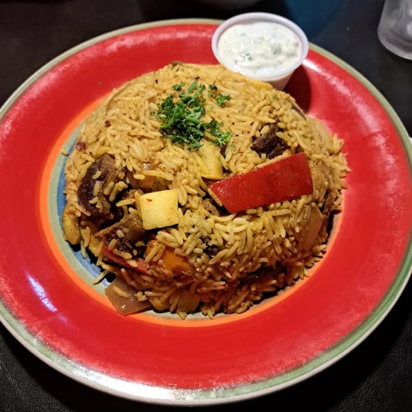 KINZI's Mediterranean rice dish with meat, vegetables, and a side of white sauce on a colorful plate.