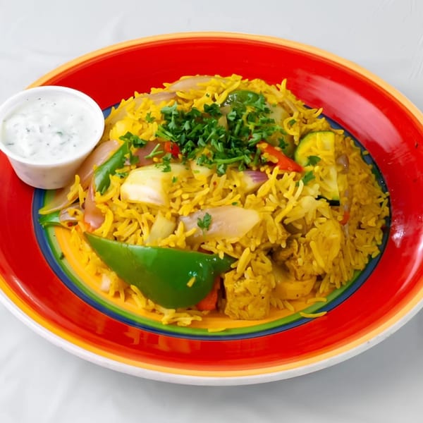 KINZI's Mediterranean rice pilaf with vegetables and a side of white sauce on a colorful plate.