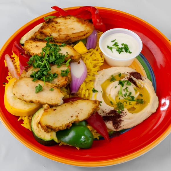 KINZI Mediterranean chicken plate with rice, vegetables, hummus, and a side of white sauce.